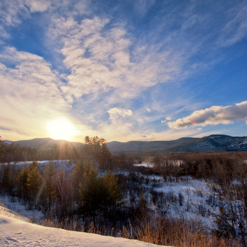 A sunrise over a a mountain with snow, blue sky and white clouds